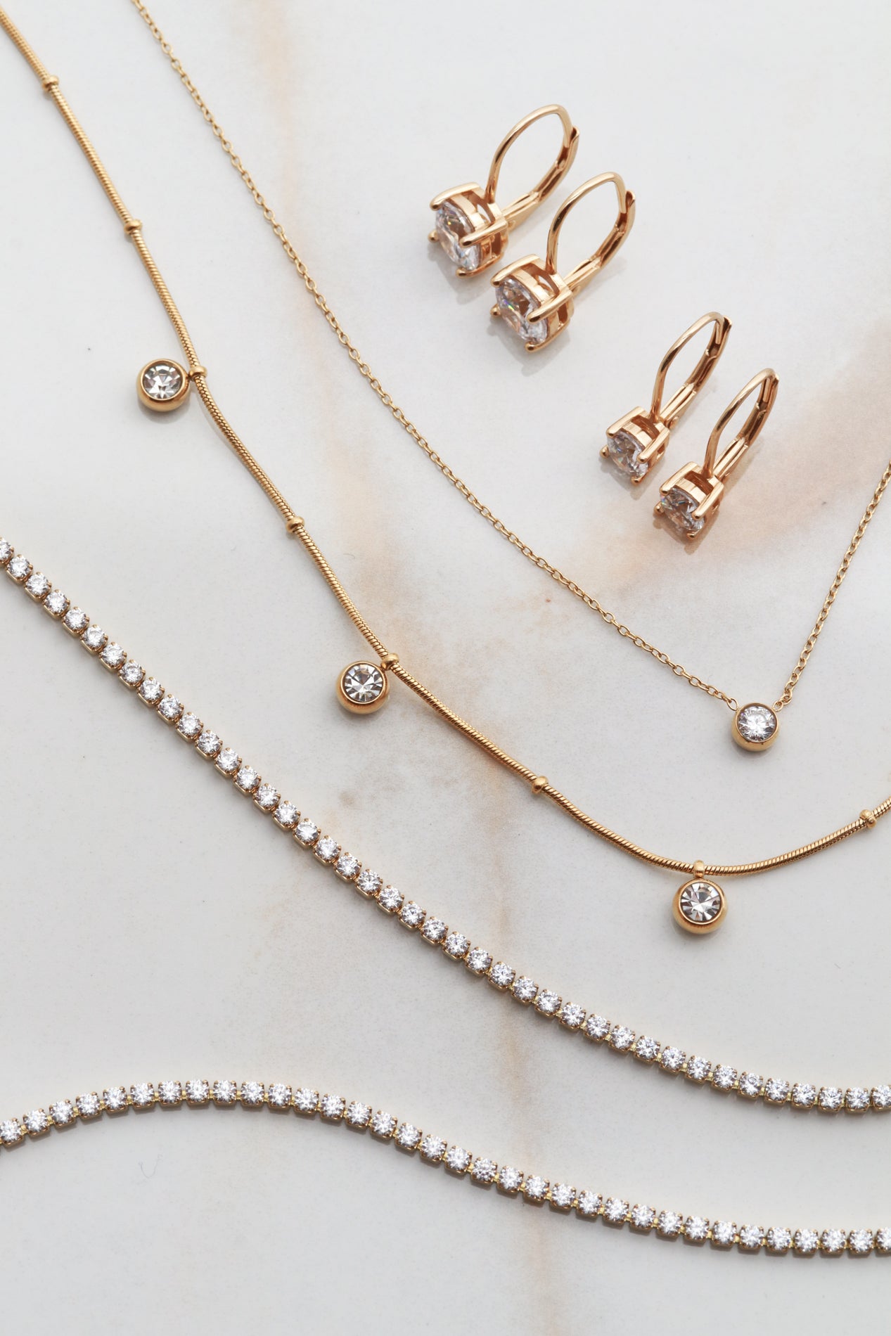 a collection of gold jewelry, including necklaces, earrings, and a bracelet, arranged on a marble surface.