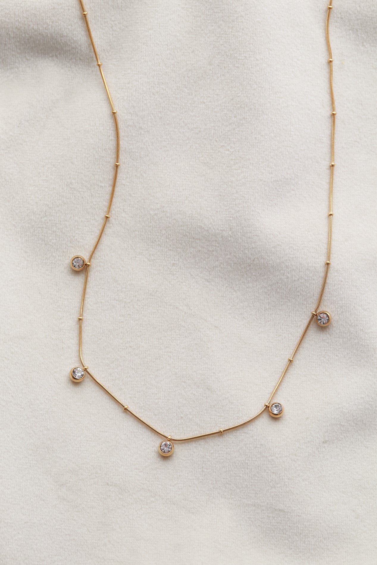 A delicate gold necklace with small diamonds hanging from it, displayed on a white fabric background.