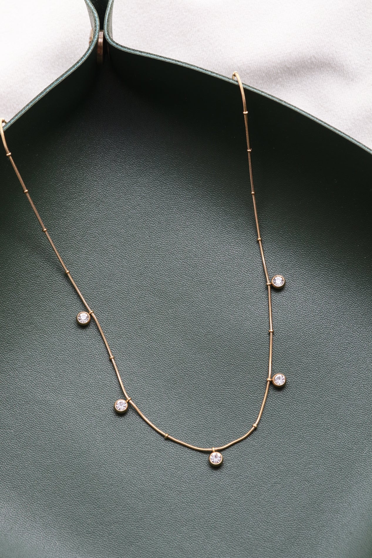 A delicate gold necklace with small round stones is displayed on a green surface.