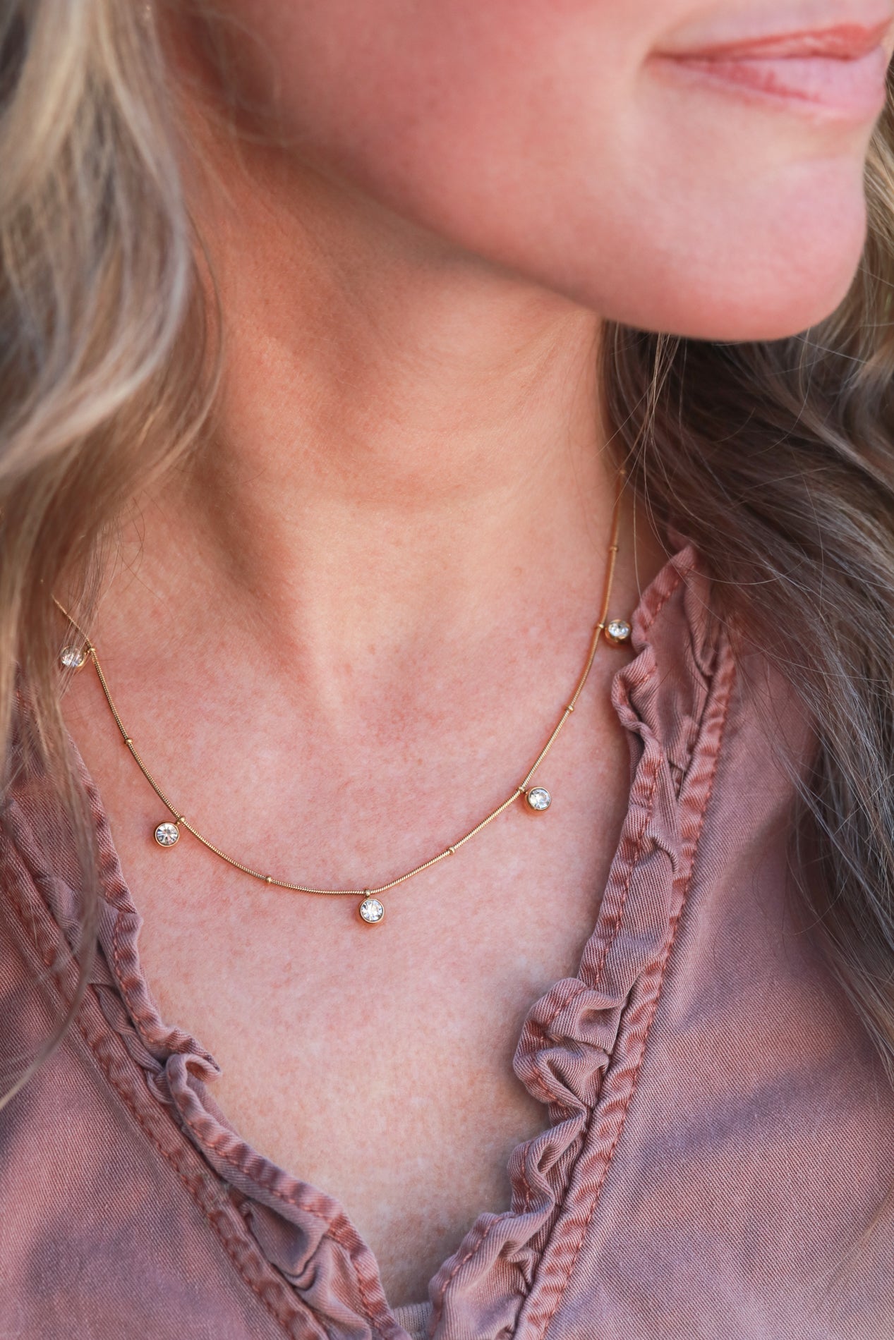 A close-up of a woman's neck and chest area, featuring a delicate gold necklace with small diamonds.