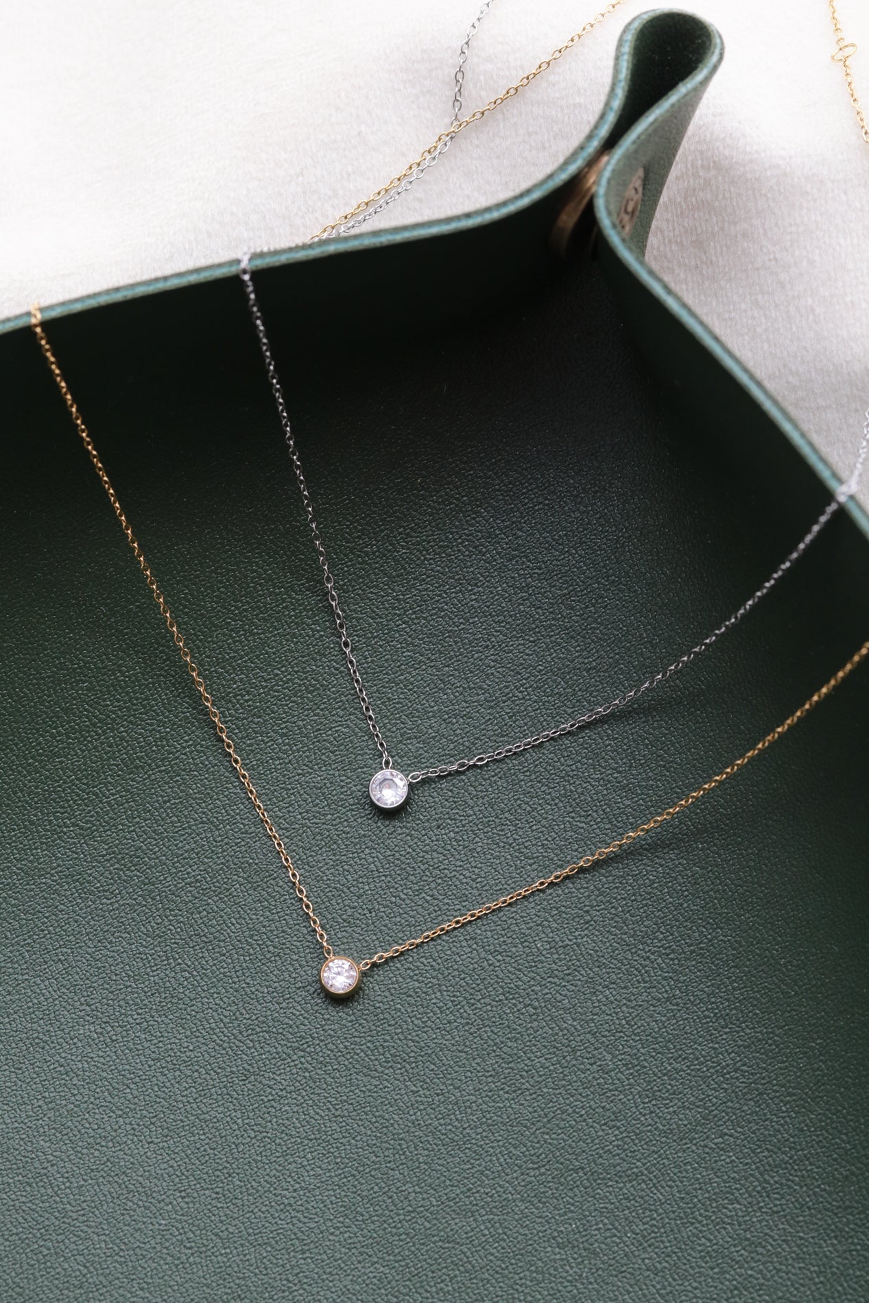 two delicate necklaces with small diamonds hanging from them, resting on a green surface.