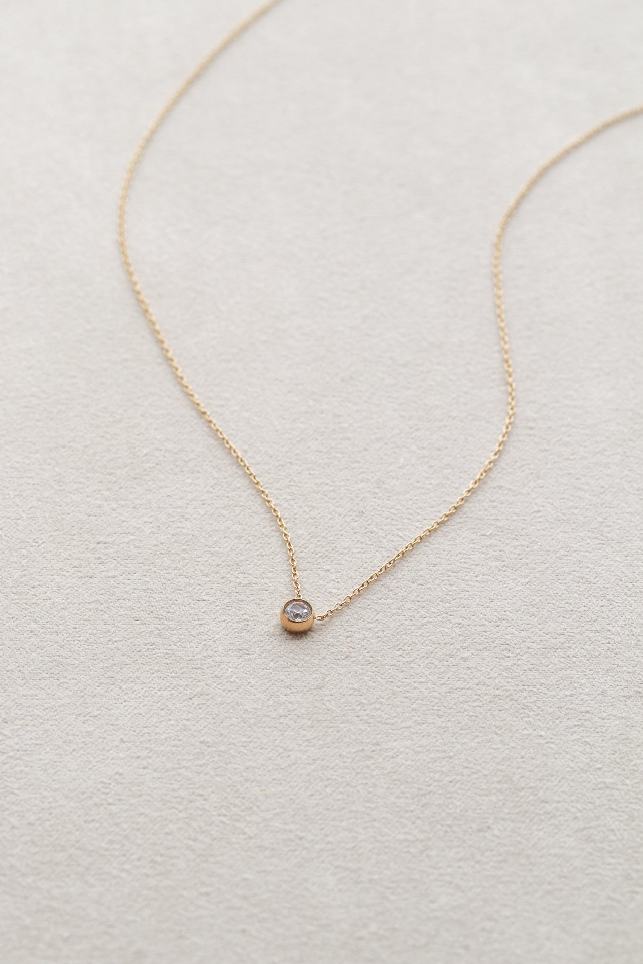 A delicate gold necklace with a small diamond pendant rests on a light-colored surface.