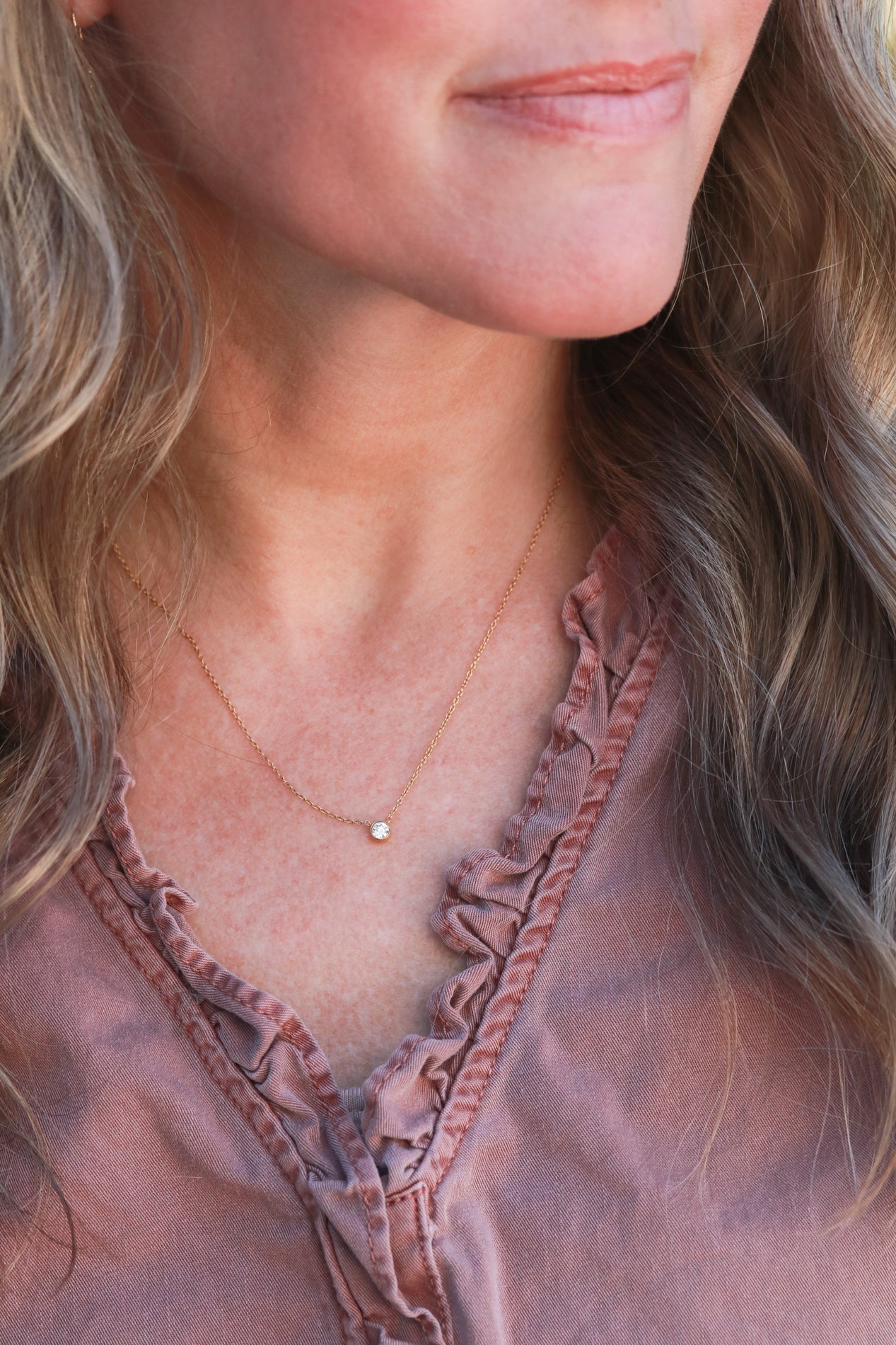 A close-up of a woman's neck and chest area, featuring a delicate necklace with a small cz solitaire pendant.