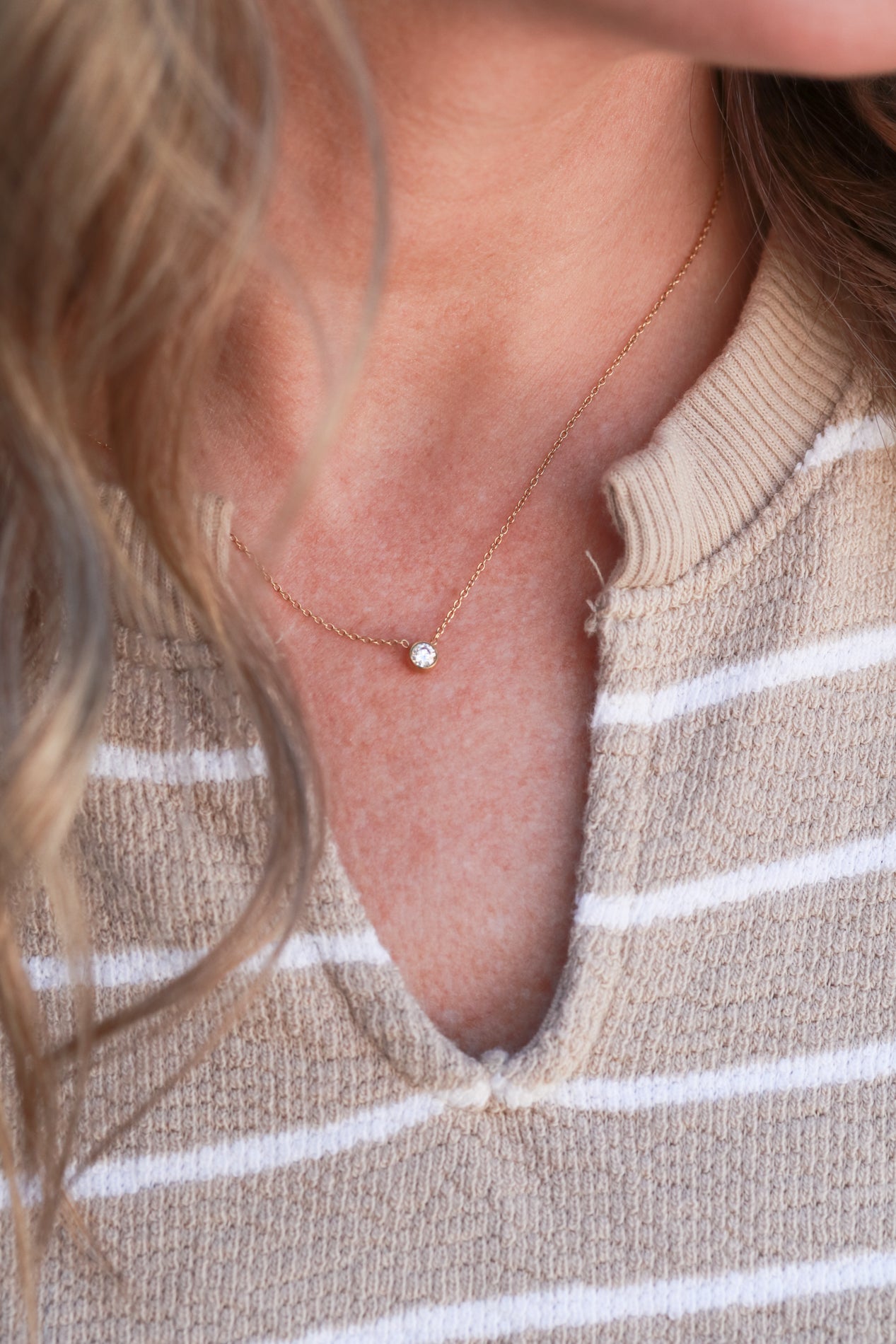 A close-up view of a person's neck and chest area, featuring a delicate gold necklace with a small diamond pendant.