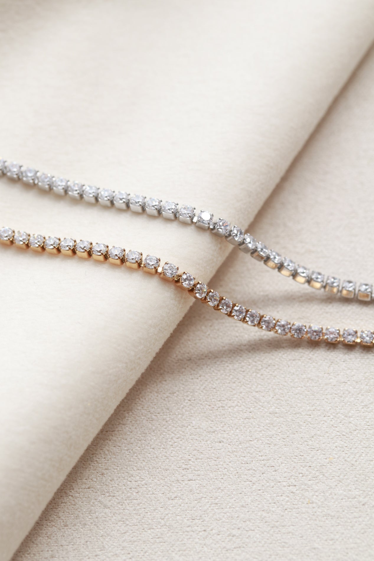 Two diamond-encrusted necklaces are displayed on a white fabric surface.