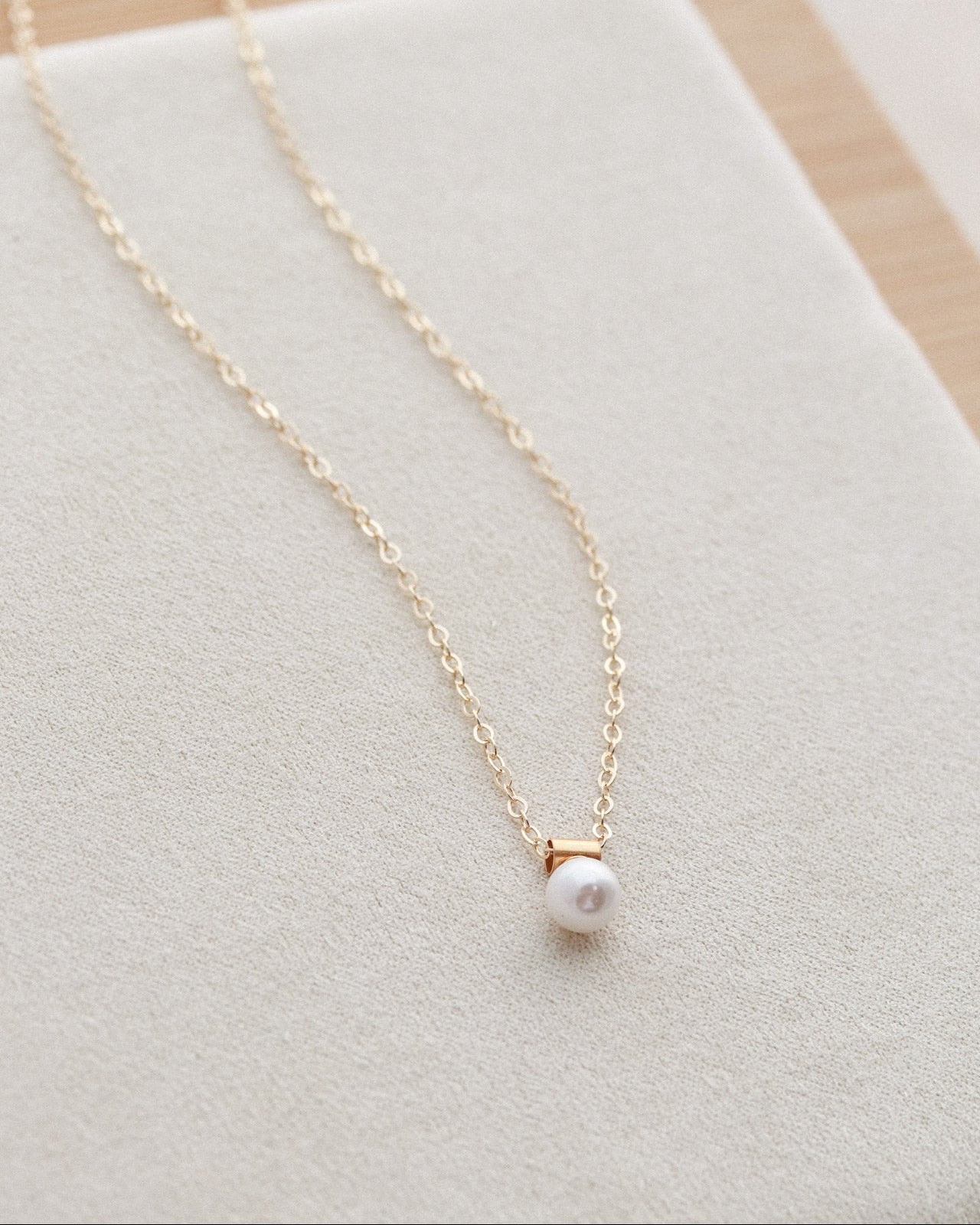 Gold necklace with a pearl pendant on a light gray surface