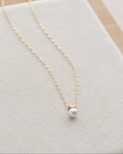 Gold necklace with a pearl pendant on a light gray surface