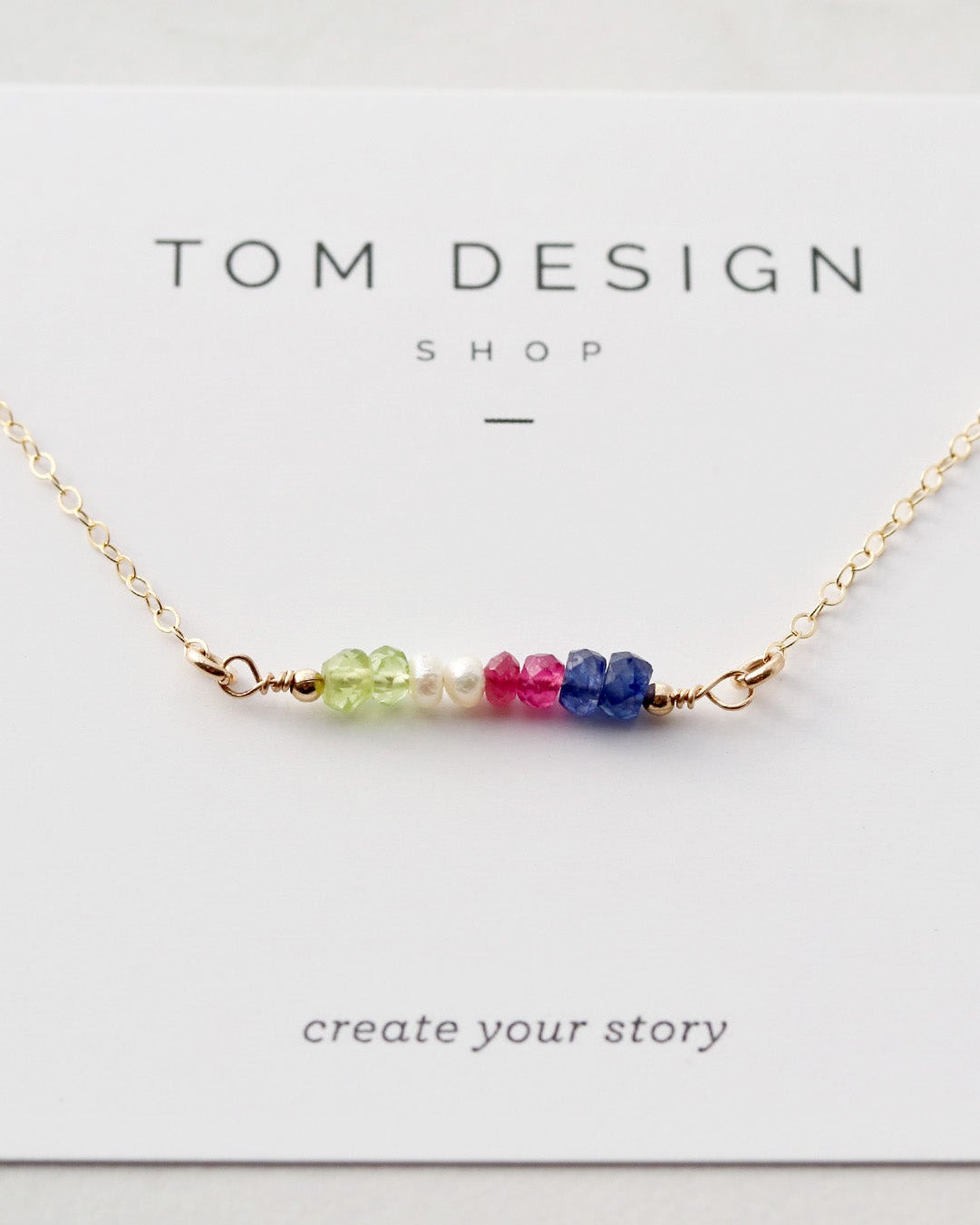 A personalized gemstone birthstone bar necklace with multiple colored gemstone beads arranged on a silver bar, presented on a white card with 'TOM DESIGN SHOP' printed at the top.