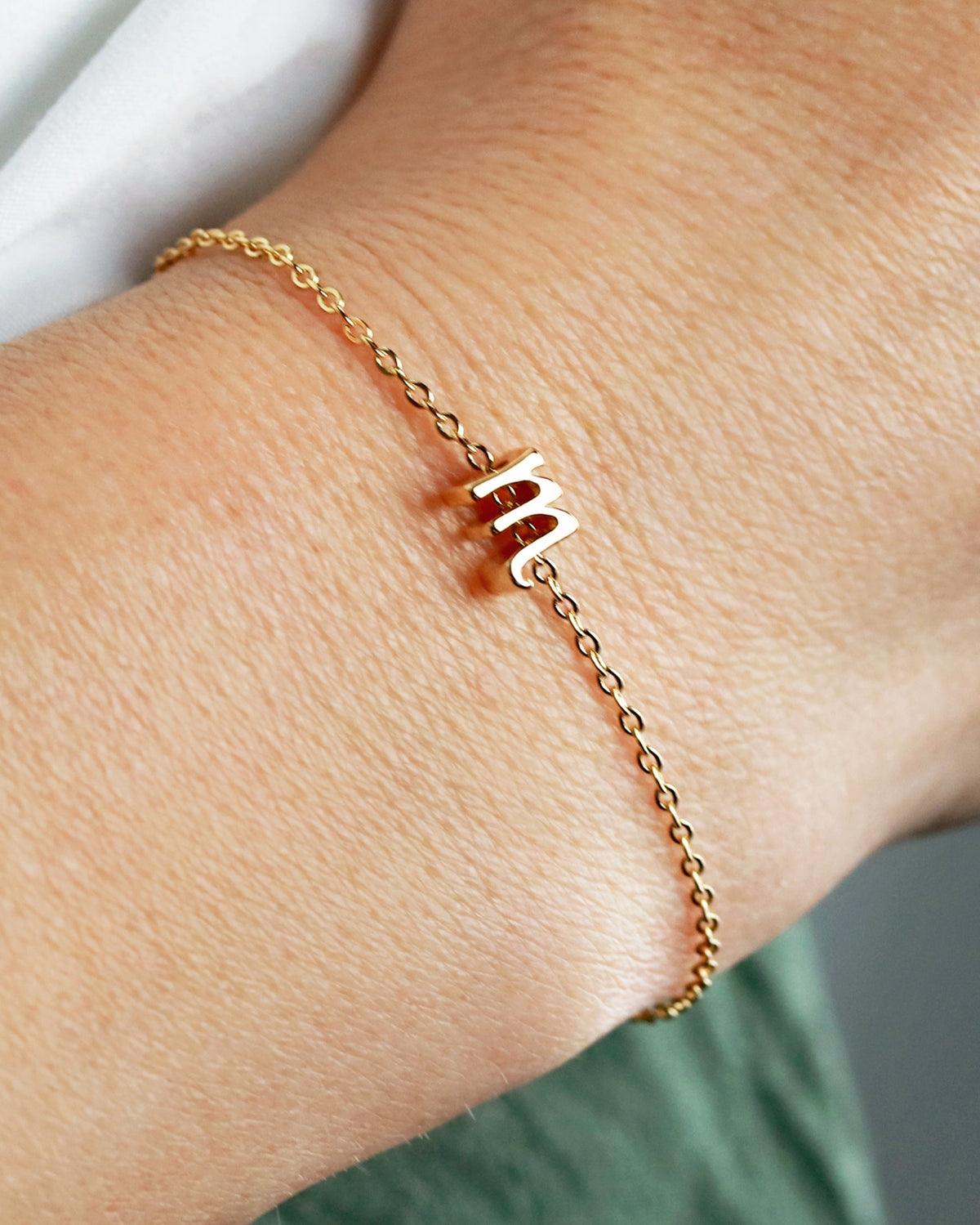 A person wearing a gold-plated chain bracelet with a single letter charm on their wrist.