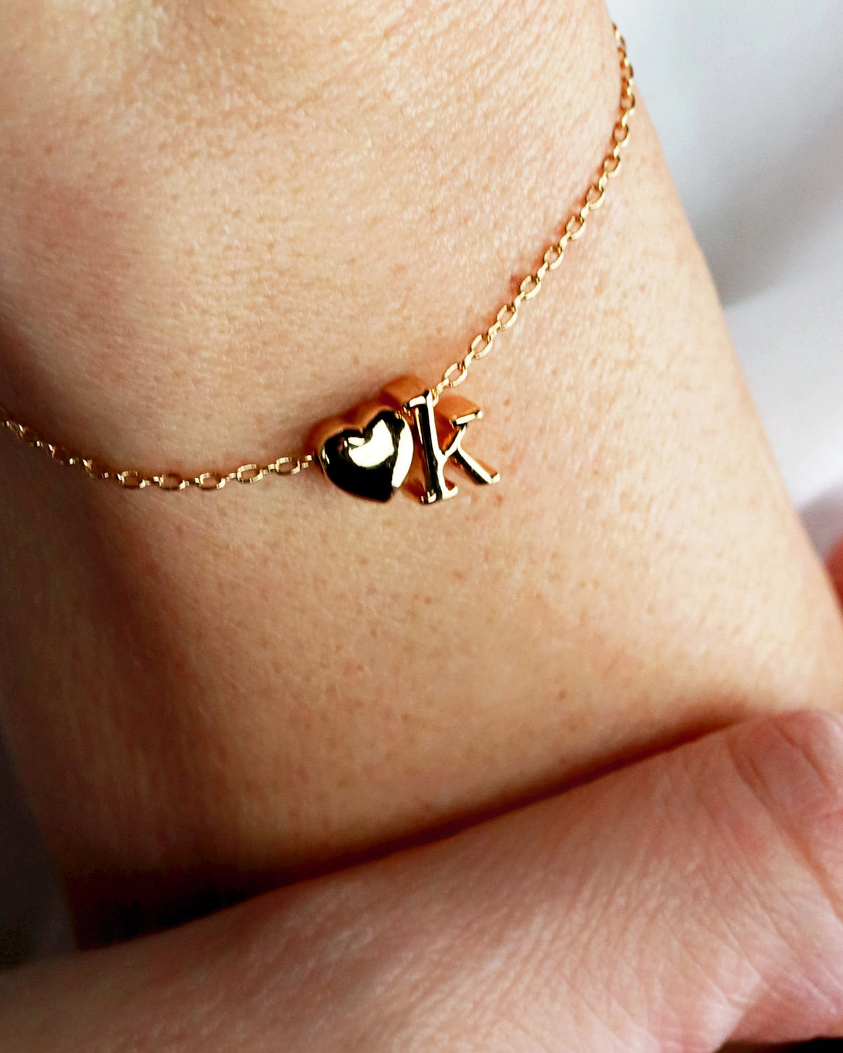 A gold-colored bracelet with two charms, one heart-shaped and one star-shaped, on a person's wrist.